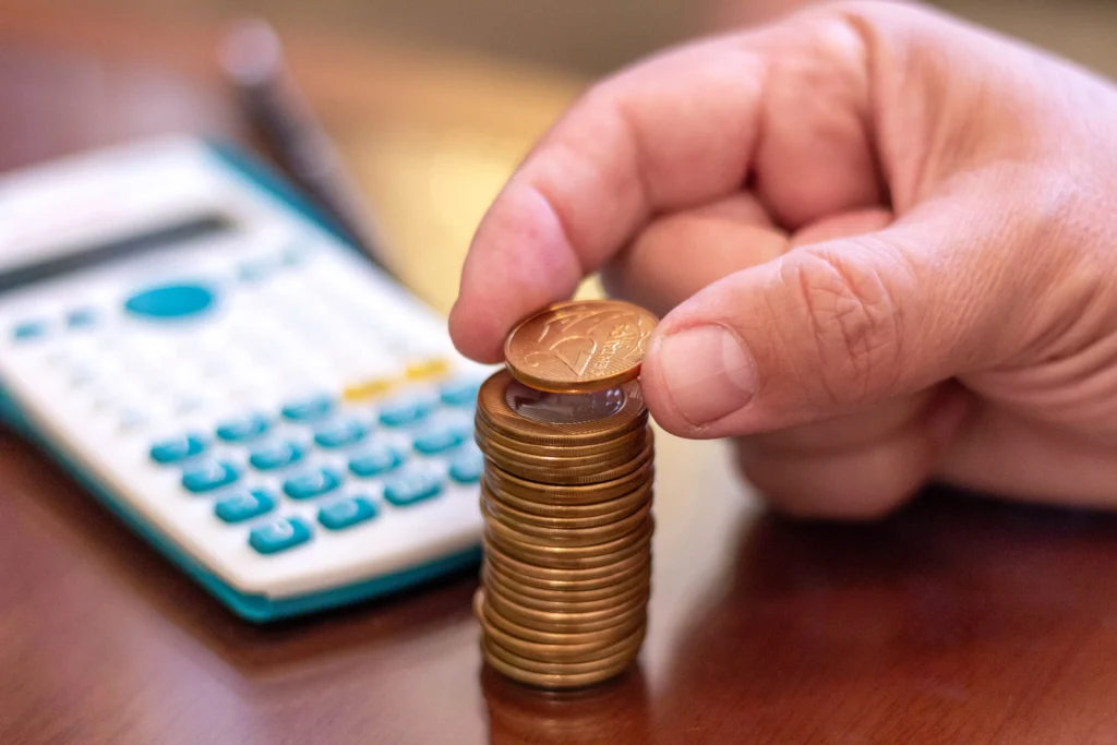 Mão empilhando moedas com calculadora ao fundo simbolizando como montar uma reserva financeira passo a passo