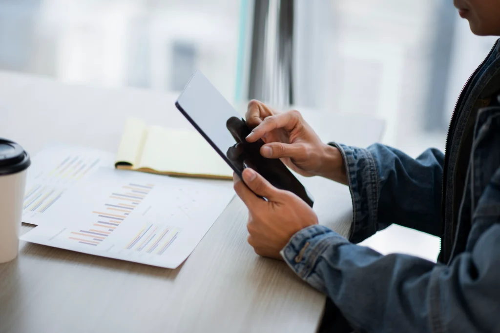 Homem usando celular com planilhas à frente para gestão de finanças pessoais procurando melhores Apps para Controle Financeiro