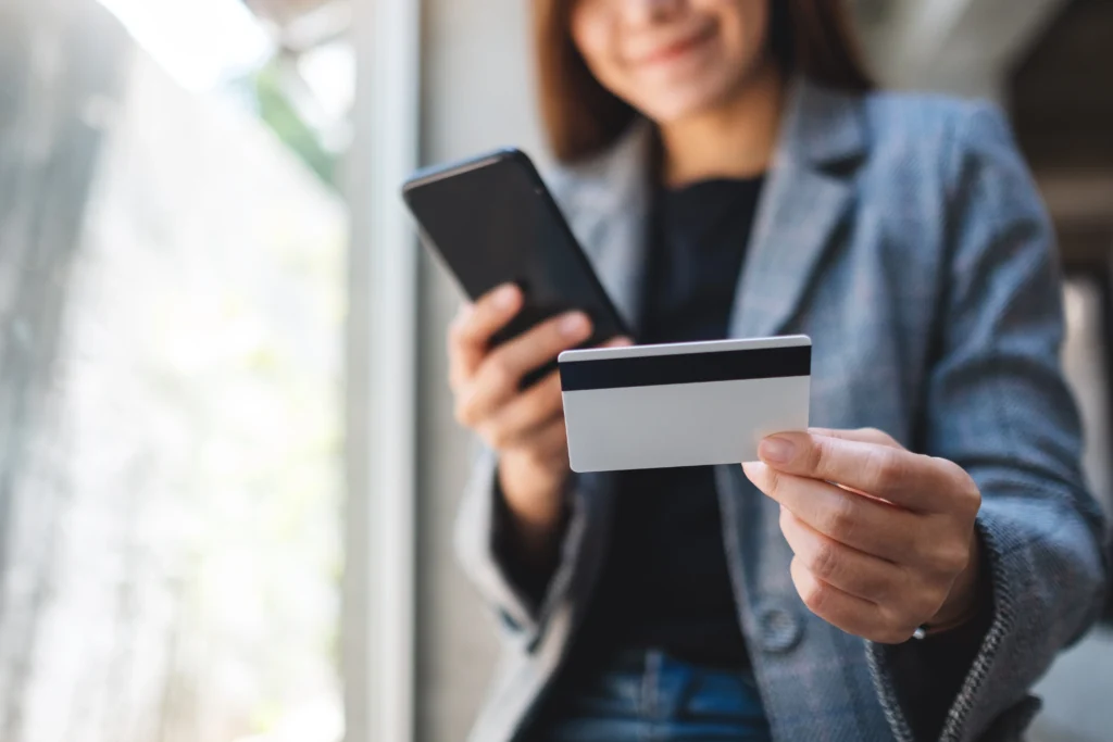 Mulher de blazer satisfeita segurando celular e cartão de crédito, simbolizando benefícios premium e compras online seguras