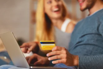 Casal feliz em casa com cartão de crédito e notebook, usando benefícios de cartões sem anuidade para organizar finanças