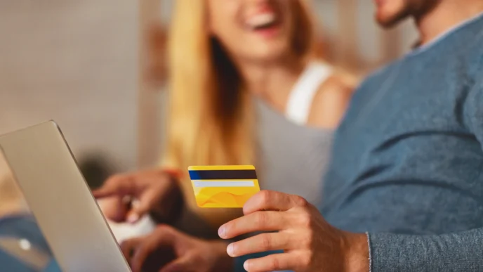 Casal feliz em casa com cartão de crédito e notebook, usando benefícios de cartões sem anuidade para organizar finanças