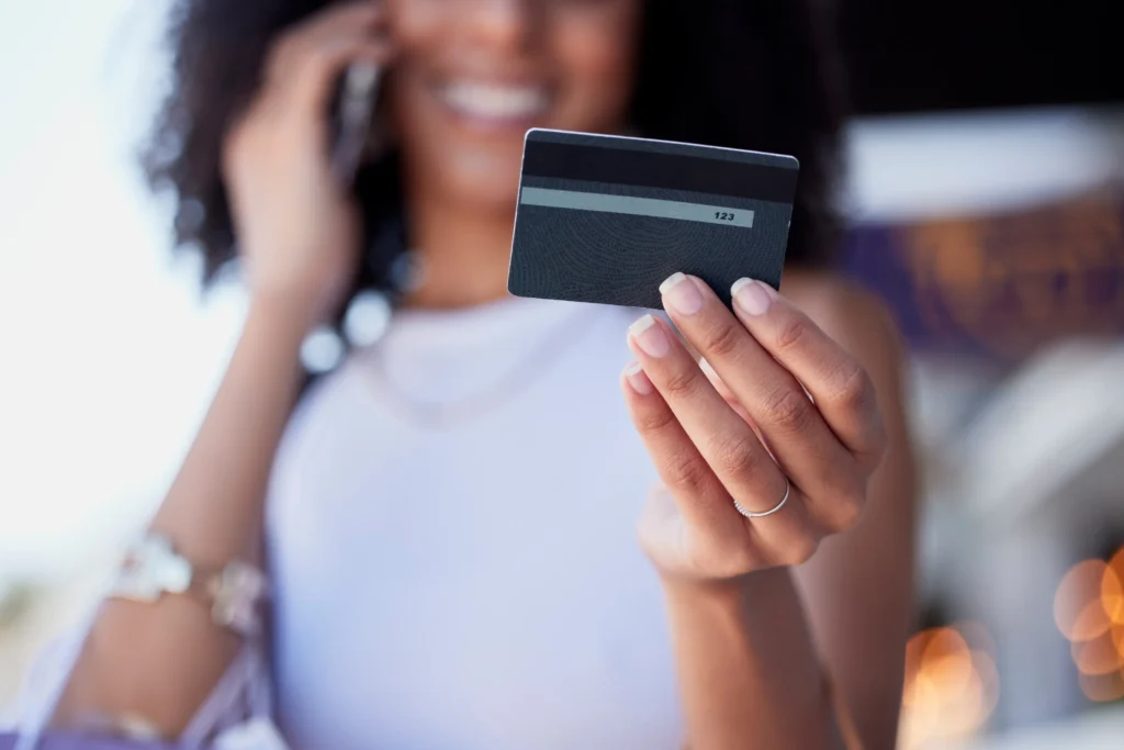 Mulher sorrindo ao celular enquanto segura um cartão de crédito, representando praticidade e aprovação rápida de cartões