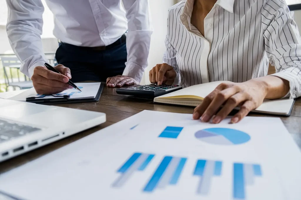 Duas pessoas analisando papéis e gráficos com calculadora e caneta, organizando gastos e investimentos financeiros