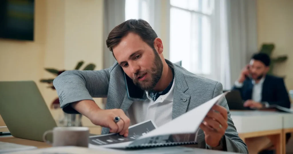 Homem atarefado falando ao celular e consultando fichário, mostrando a rotina confusa sem apoio de um profissional financeiro