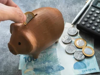 Pessoa guardando dinheiro em cofrinho ao lado de calculadora, simbolizando planejamento e análise de investimentos pessoais.